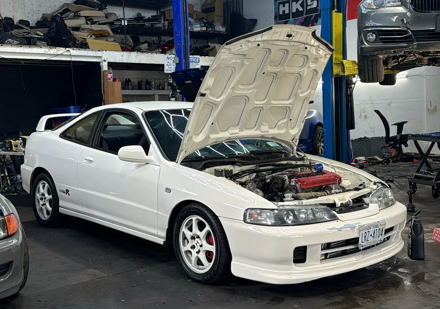 White JDM performance coupe in the shop with the hood open during repair work