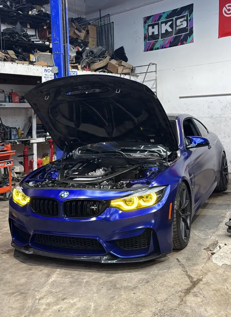 Blue BMW in the shop with the hood open during diagnostics, cropped to show the full vehicle with minimal background
