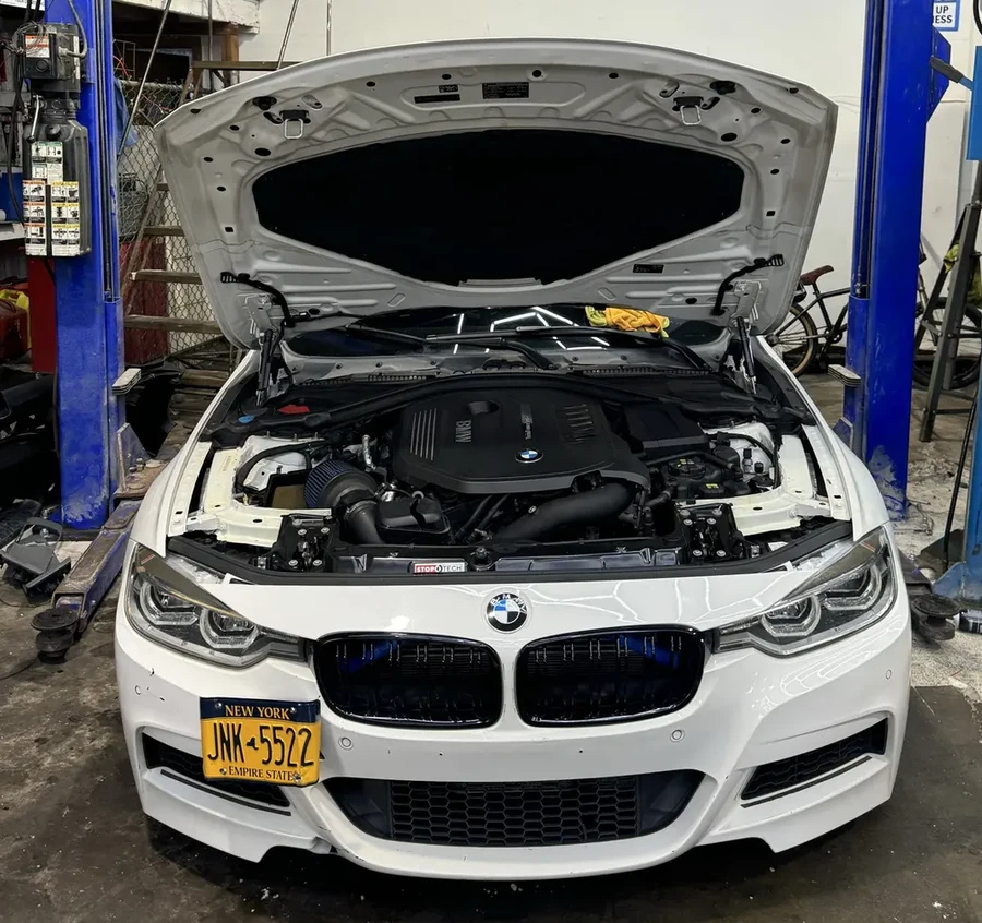 White BMW with hood open on a service lift showing the full front of the vehicle and engine bay