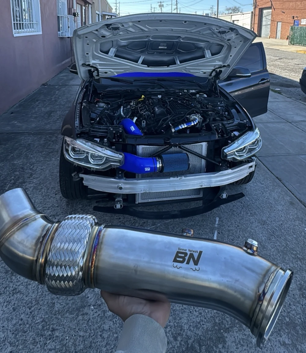 BMW performance build with the front bumper removed and an exhaust component held in front of the car