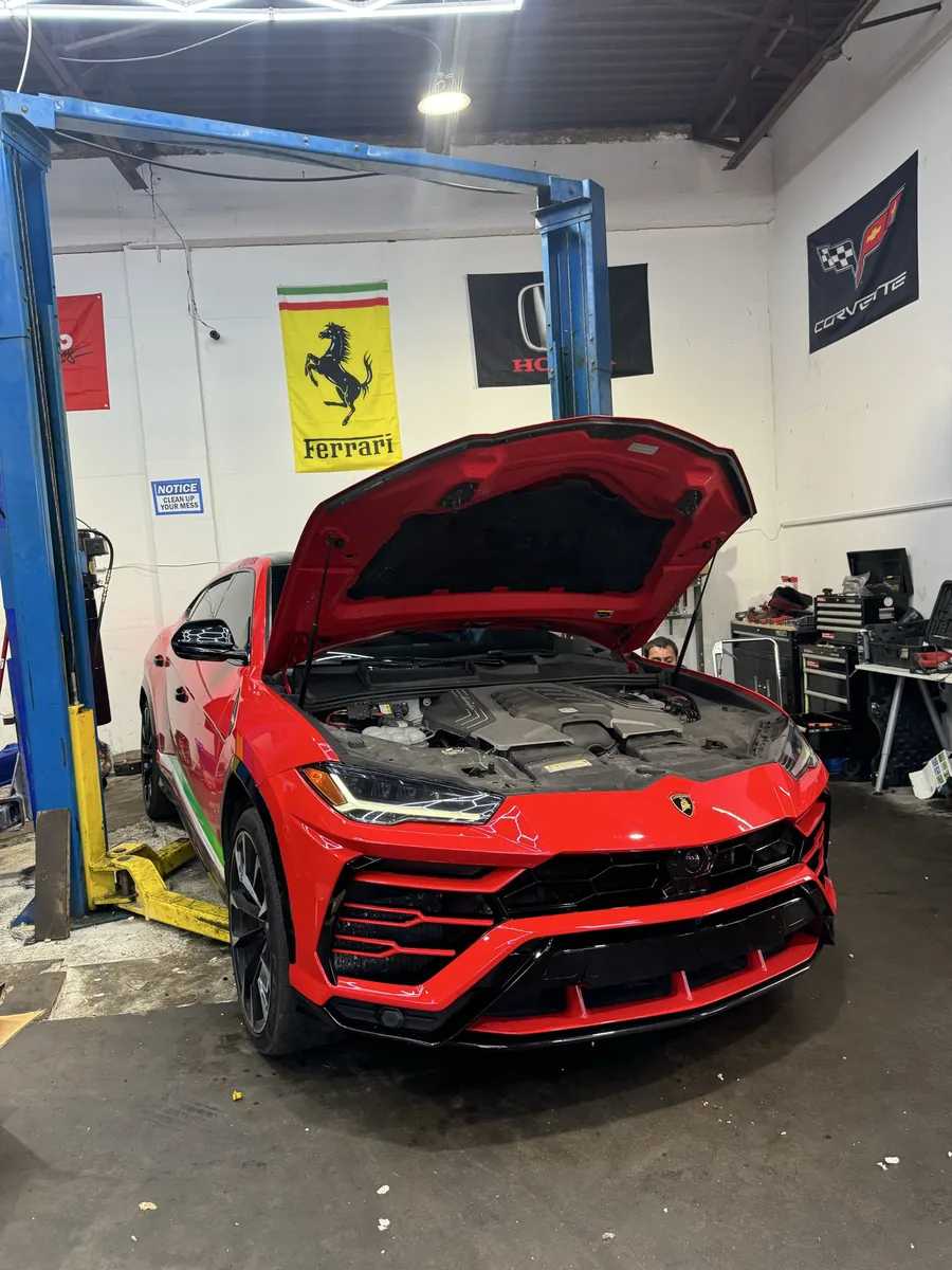 Red Lamborghini Urus in the shop with the hood open during maintenance service