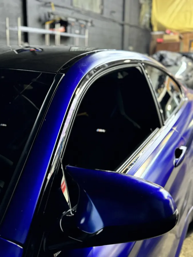 Close-up of a freshly tinted side window on a dark blue car reflecting overhead shop lights